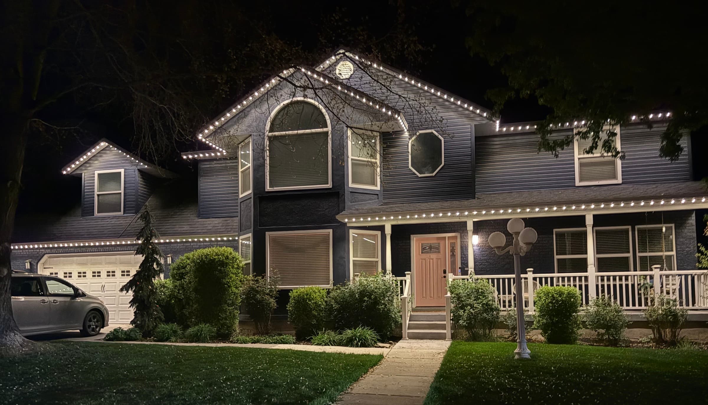 Two-story home at night with warm white permanent holiday lights installed by Ekko Lighting