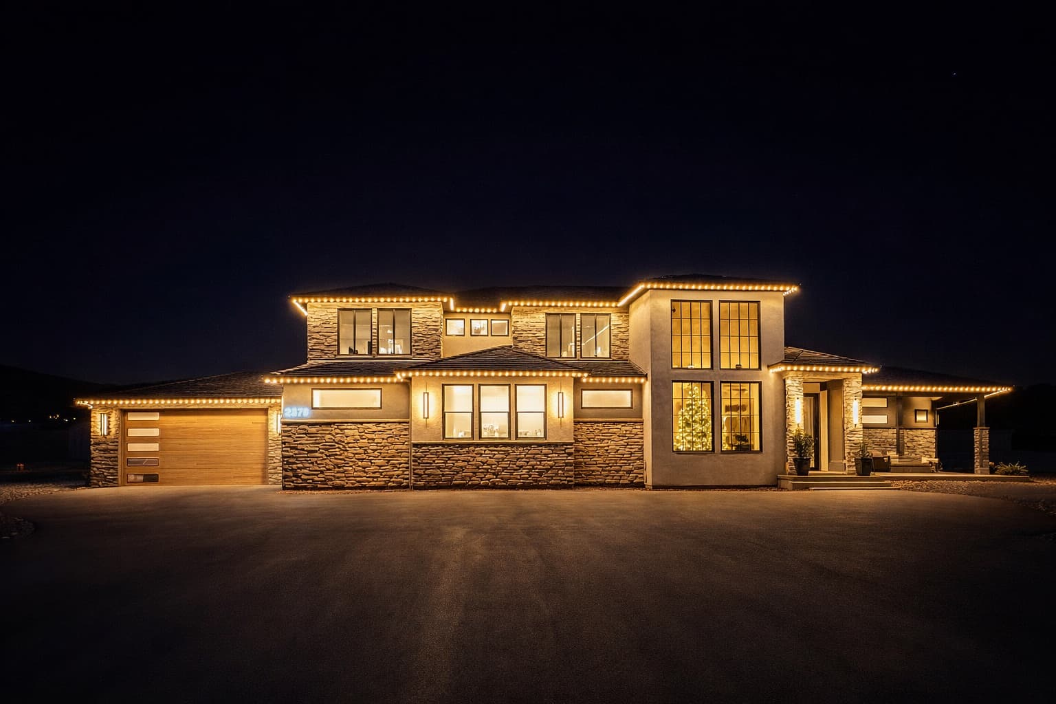 Modern stone home at night with amber permanent lights along every roofline